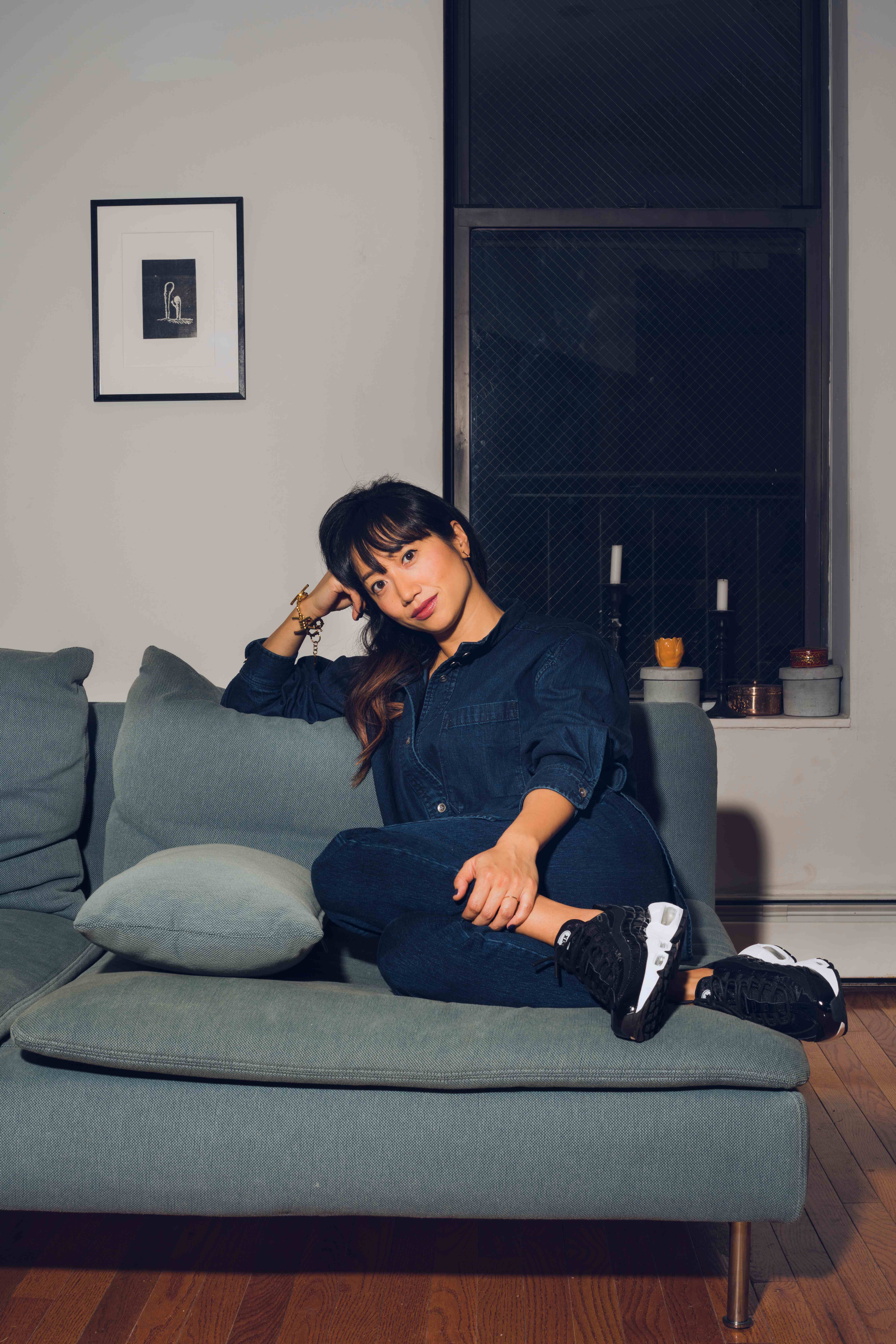 Jamie Nami Kim sitting thoughtfully on a couch in a modern interior